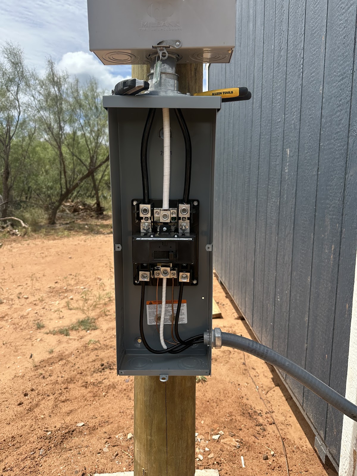 Service entrance panel mounted on a pole in red Texas dirt